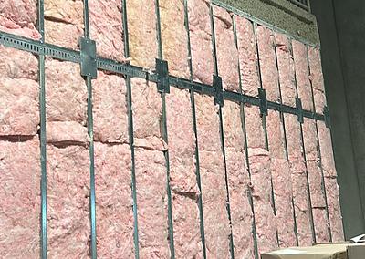 Pink batt insulation packed tight between steel studs behind horizontal resilient channel.