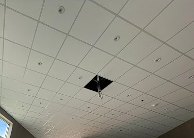 A suspended T-bar grid carrying lay-in acoustic tile and recessed pot lights, with one tile left out at a hanger wire.